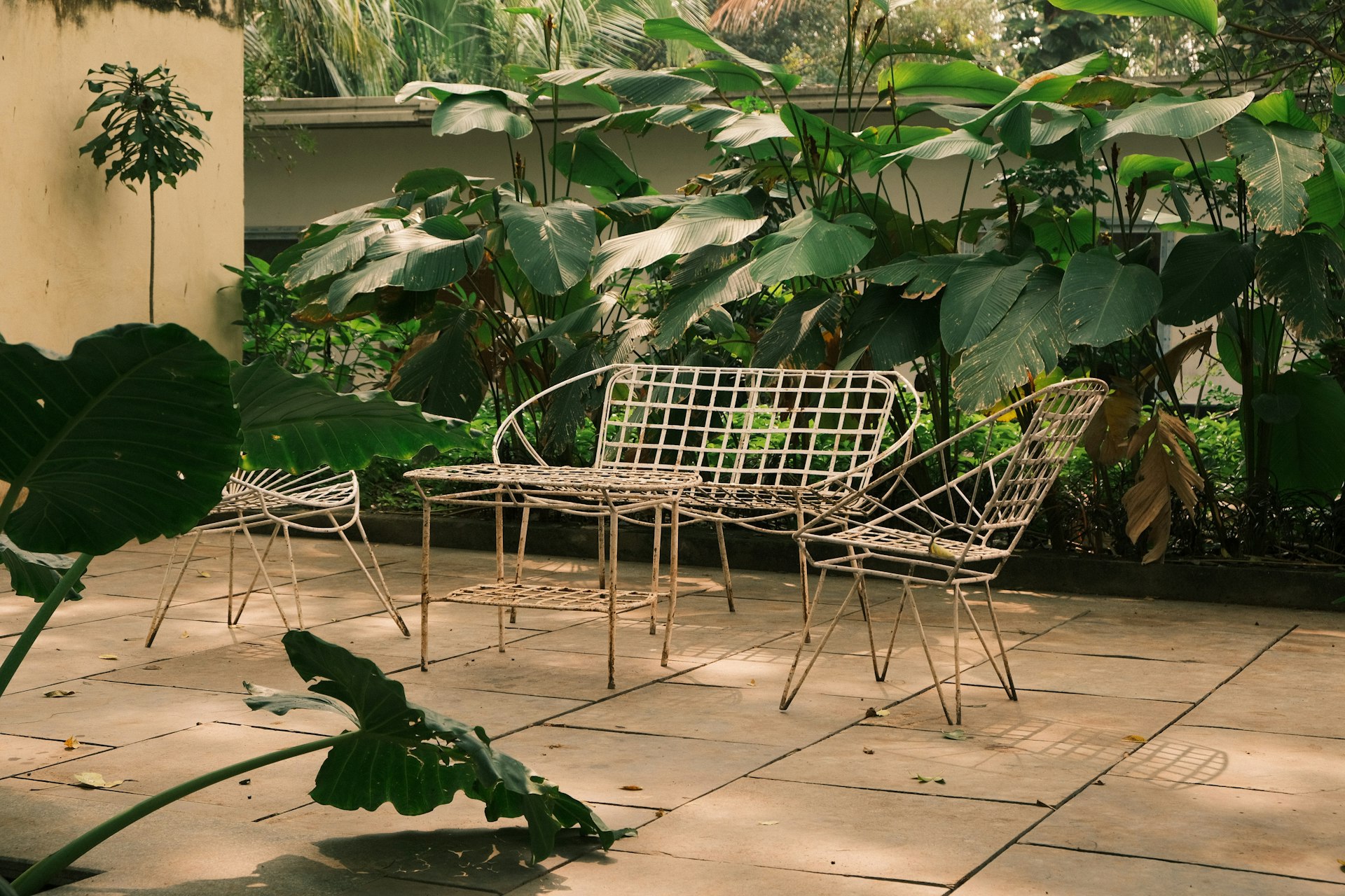 White metal patio furniture set surrounded by lush greenery.